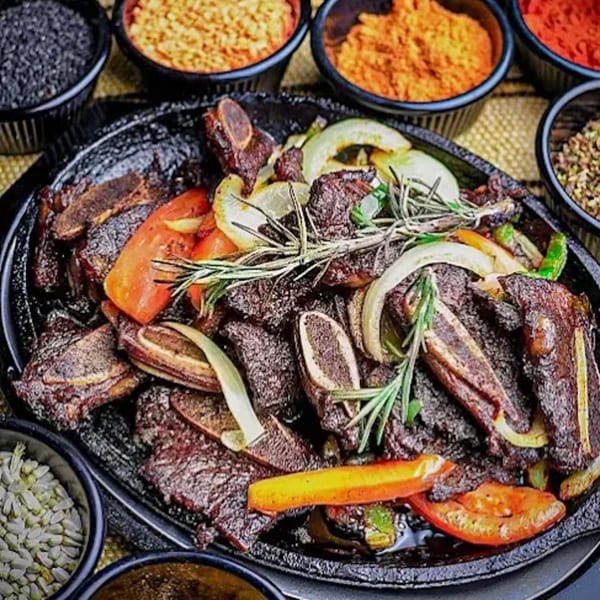 Ethiopian lamb tibs with peppers, onions, and rosemary, surrounded by bowls of spices.