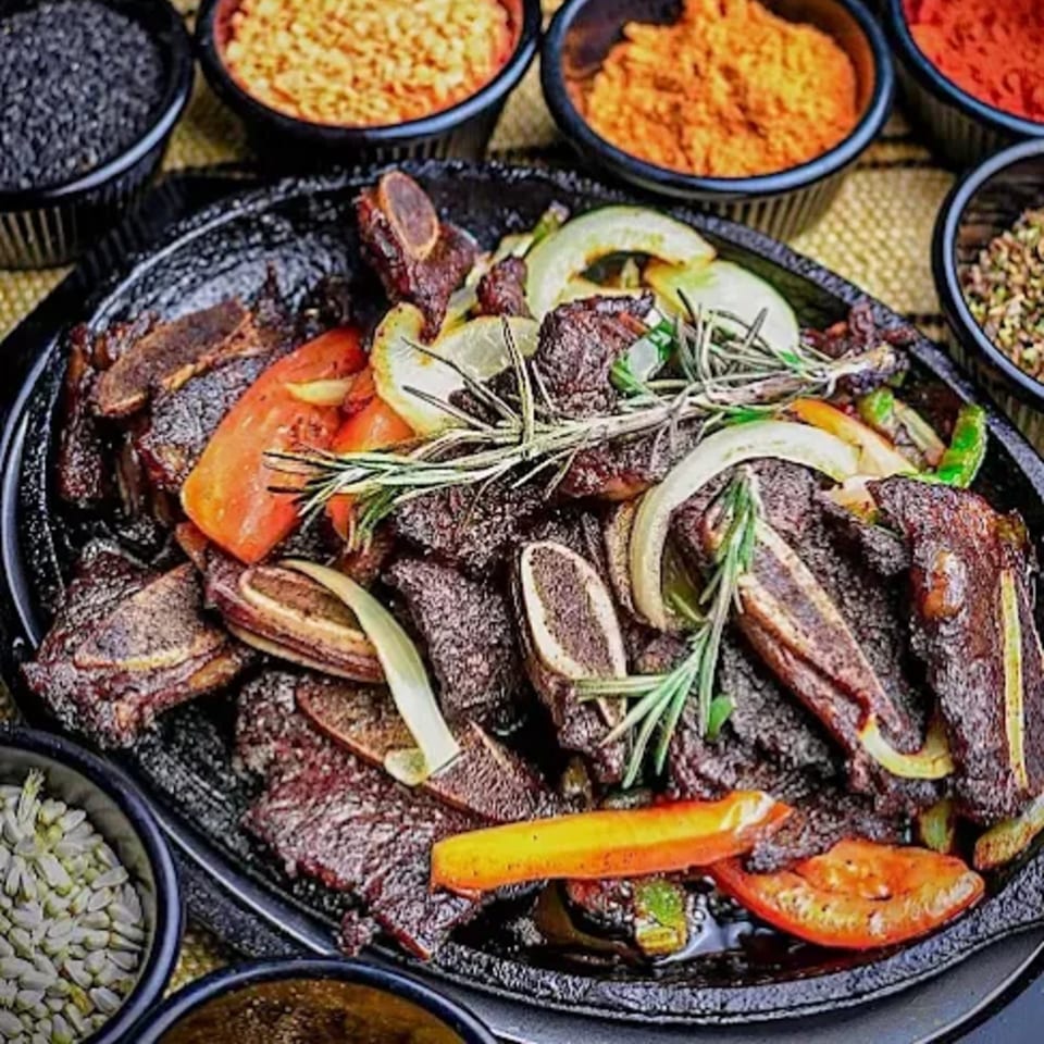Ethiopian lamb tibs with peppers, onions, and rosemary, surrounded by bowls of spices.