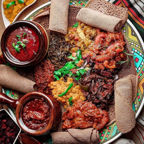 A colorful platter of various Ethiopian stews, vegetables, and injera bread rolls.