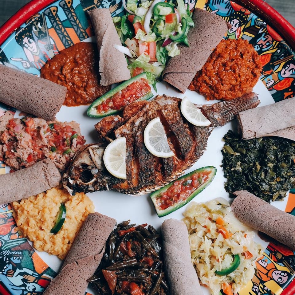 Bahel Ethiopian Restaurant's large platter of injera, whole fried fish, and various colorful stews and vegetables.