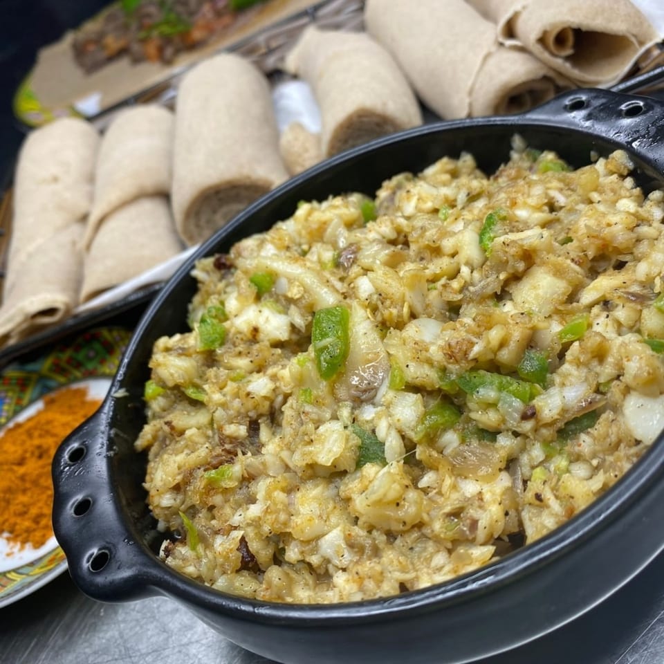 A black bowl of Ethiopian scrambled eggs with green peppers, alongside rolled injera bread.